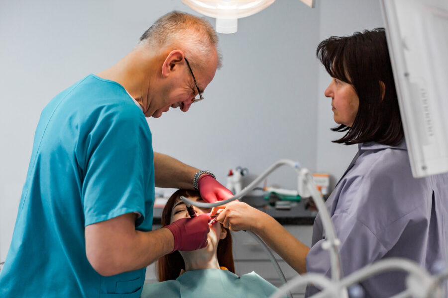 Closeup portrait of Old Senior man dentist and his assistant doing treatment operation in the dental office for young woman patient. Dentistry, tooth pain concept.